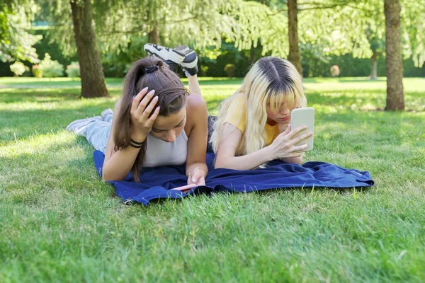 Две молодые девушки-подростки лежат на траве в парке со смартфонами — стоковое фото