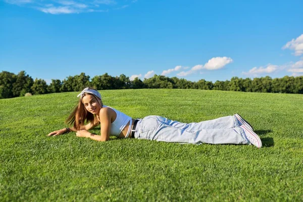 Flicka hipster tonåring som ligger på gräs, grön gräsmatta och blå himmel bakgrund Stockbild