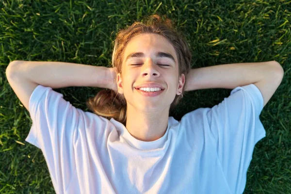 Close-up gezicht van knappe jongen 16, 17 jaar oud op groen gras, top uitzicht — Stockfoto