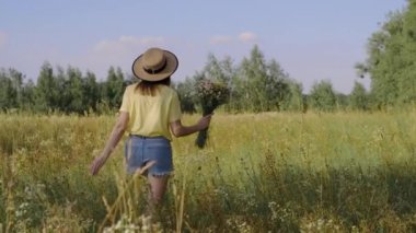 Bir buket kır çiçeğiyle gezen ve çayırda çiçek toplayan mutlu bir kadın.