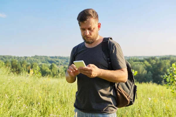 Middle-aged bearded man with backpack using smartphone — Stock Photo, Image