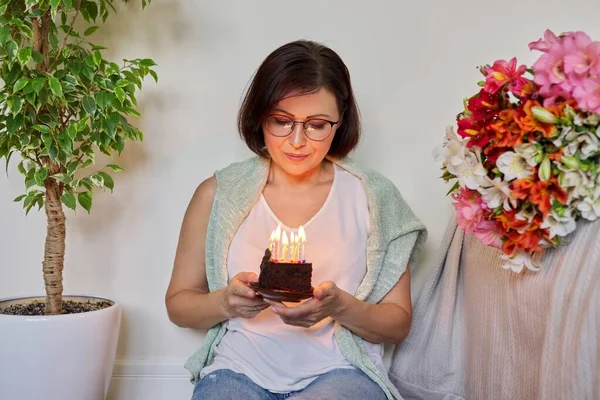 Cumpleaños, celebración, aniversario, mujer de 45 años con un pequeño pastel con velas encendidas —  Fotos de Stock