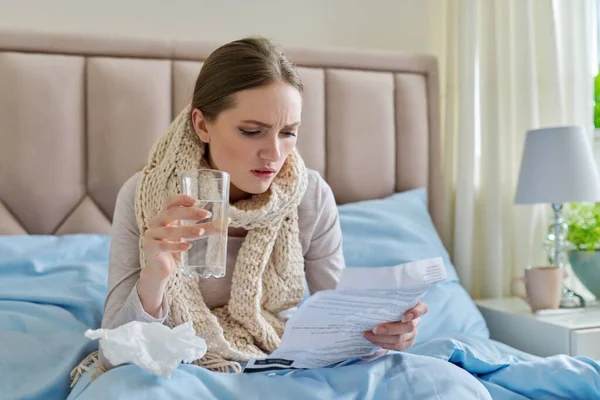 Ung sjuk kvinna hemma i sängen, kvinnlig läsning instruktioner för medicinering — Stockfoto