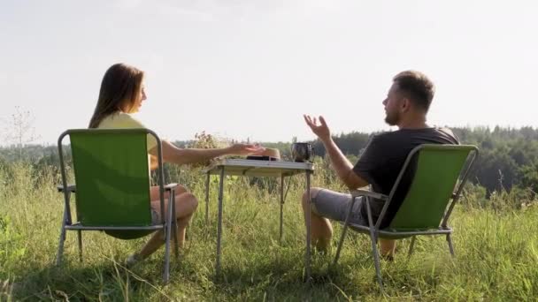 Пара средних лет отдыхает на природе, сидит на открытых стульях — стоковое видео