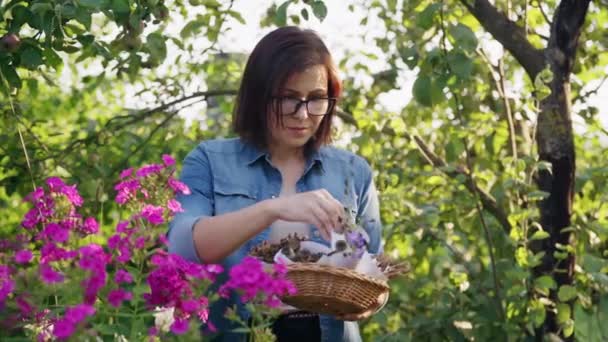 Nainen kesäpuutarhassa kerättyjen kuivattujen kukkien kanssa kasvien siemenet korissa — kuvapankkivideo