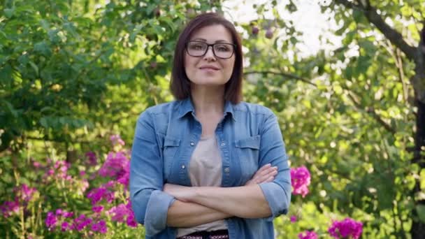 Portret van een zelfverzekerde vrouw van middelbare leeftijd met gekruiste armen in de tuin — Stockvideo