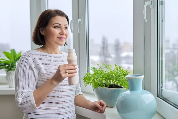 Frau mittleren Alters trinkt Milchprodukte, Joghurt, Milch in der Flasche — Stockfoto