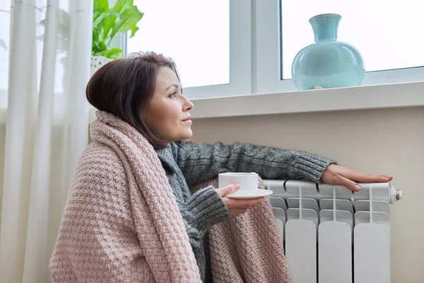 Зимовий сезон, жінка розігрівається біля радіатора опалення будинку — стокове фото