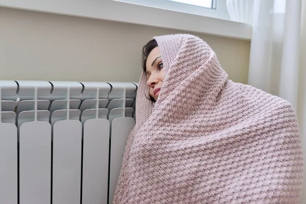 Зима, отопительный сезон. Женщина в теплом свитере сидит в домашней комнате рядом с отопительным радиатором — стоковое фото