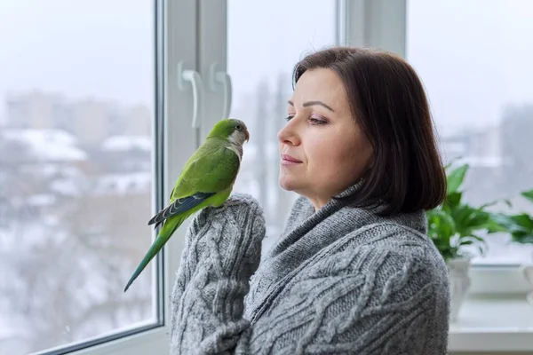 Mujer de mediana edad y loro juntos, propietaria de un pájaro hablando mirando a la mascota del cuáquero verde — Foto de Stock