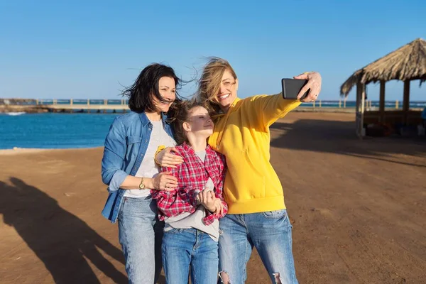 Heureux deux femmes d'âge moyen et fille enfant prenant selfie sur smartphone, fond de plage de la mer — Photo