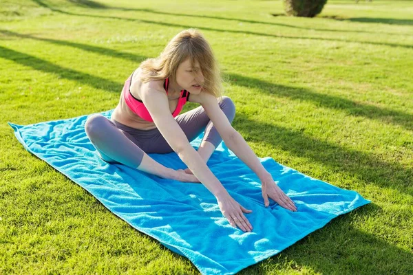 Middle-aged active woman doing sports exercises on a rug on the grass, in the morning. — Stock Photo, Image