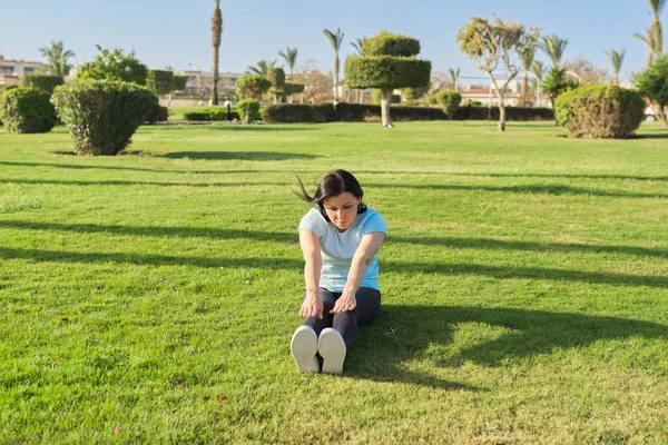 Middle-aged woman doing outdoor sports, 40s female sitting on grass on sunny summer morning — Stock Photo, Image