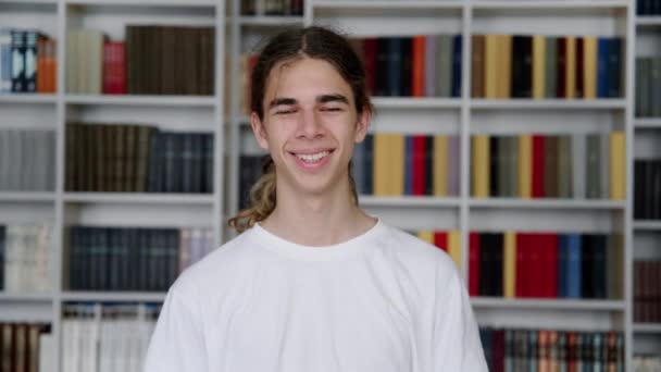 Single portret van glimlachende zelfverzekerde mannelijke student tiener kijken naar de camera in de bibliotheek — Stockvideo