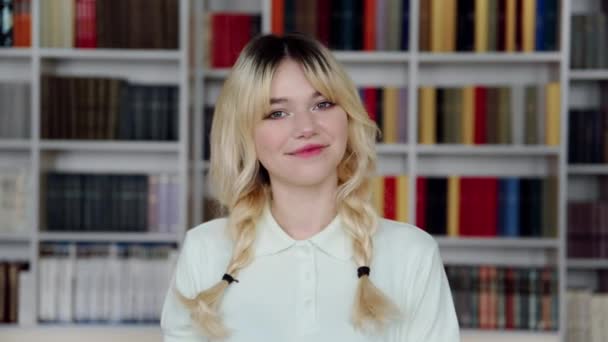 Retrato de una estudiante adolescente sonriente mirando a la cámara, fondo interior de la biblioteca — Vídeo de stock