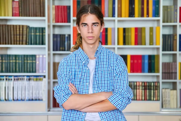 Einzelporträt eines ernsthaften selbstbewussten männlichen Teenagers, der in der Bibliothek in die Kamera blickt — Stockfoto