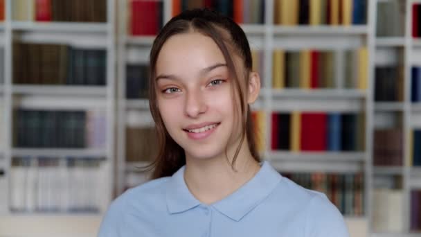 Portret van lachende vrouwelijke tiener student op zoek naar camera, bibliotheek interieur achtergrond — Stockvideo