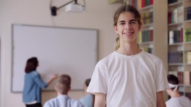 Portrét usmívajícího se sebevědomého studentského teenagera dívajícího se do kamery v knihovně — Stock video