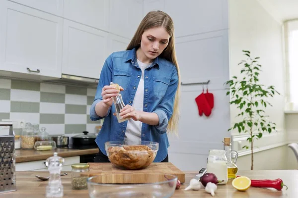 Молода жінка готує курку, маринує зі спеціями чорний перець сіль, вдома на кухні — стокове фото