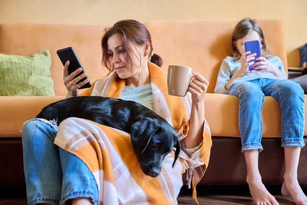 Mutter, Tochter und Hund sitzen zu Hause auf der Couch und schauen auf den Smartphone-Bildschirm — Stockfoto