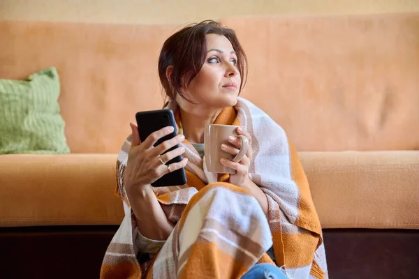 Herbst-Winter-Porträt einer Frau mittleren Alters unter warmer Decke mit Tasse und Smartphone — Stockfoto