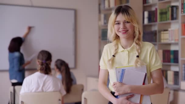 Portret van lachende vrouwelijke tienerstudent kijkend naar camera met leerboeken — Stockvideo