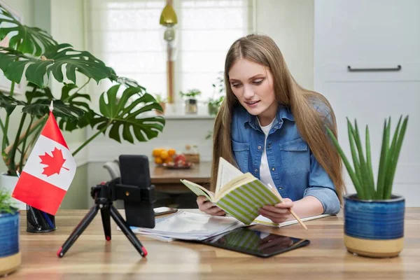 Онлайн-навчання, підліток-жінка сидить вдома, дивлячись на екран смартфона, на настільний канадський прапор — стокове фото