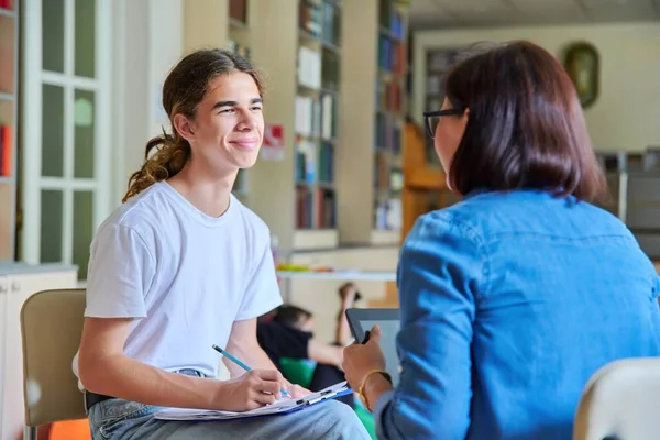 Kobieta szkoła psycholog nauczyciel mówi i pomaga student, mężczyzna nastolatek — Zdjęcie stockowe