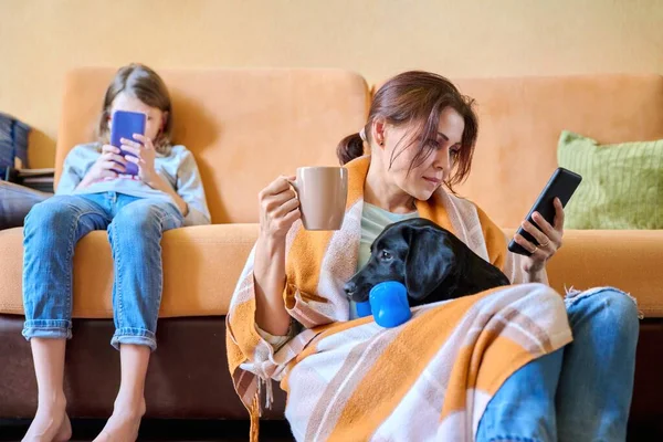 Mutter, Tochter und Hund sitzen zu Hause auf der Couch und schauen auf den Smartphone-Bildschirm — Stockfoto
