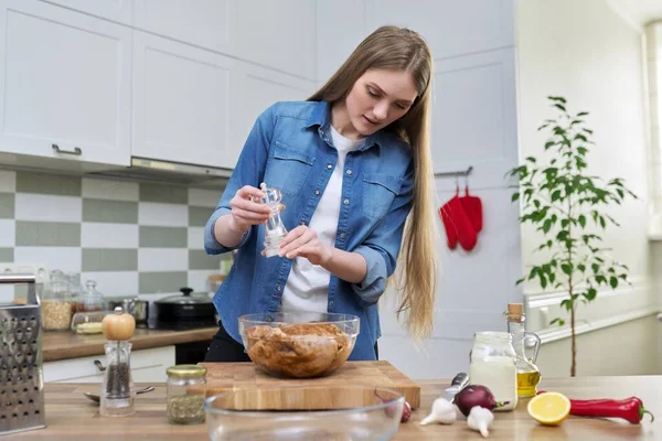 Молодая женщина готовит курицу, маринуясь со специями черного перца соль, дома на кухне — стоковое фото