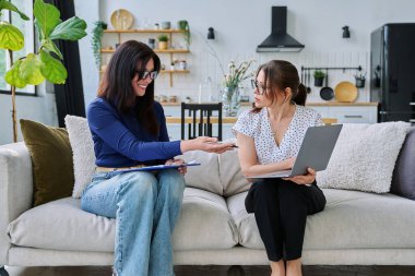 Kadın sosyal hizmet görevlisi, ruh sağlığı uzmanı orta yaşlı bir kadınla görüşüyor, oturma odasındaki kanepede yan yana oturuyor. Sosyal hizmetler, psikoloji, destek, yardım, insan kavramı