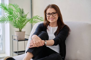 Orta yaşlı, güzel bir kadının portresi. Kanepede oturuyor. Gözlüklü, çekici, olgun bir kadın. Güzellik, sağlık, yaşam tarzı, insan kavramı