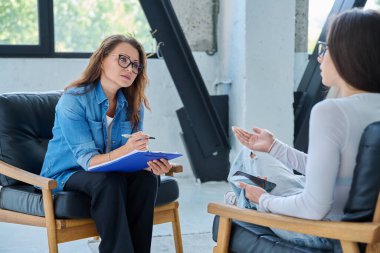 Orta yaşlı, kendine güvenen profesyonel kadın psikolog psikoterapist danışman ofiste birlikte oturan genç bir kadınla çalışıyor. Psikolojik hizmetler, bireysel terapi desteği