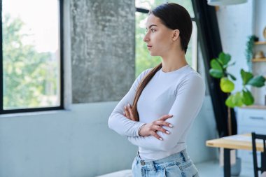 Evde poz veren güzel genç bir kadının portresi, fotokopi alanı. 17-18 yaşlarında şık bir genç kız pencereye bakıyor. Gençler için güzellik, gençlik, yaşam tarzı, ürünler ve hizmetler