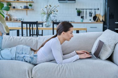 Evinde dizüstü bilgisayarla kanepede yatan genç bir kadının portresi. Üniversite öğrencisi sınava hazırlanıyor, bilgisayar başında yazı yazıyor, sosyal medya blogunu okuyor, internetten alışveriş yapıyor.
