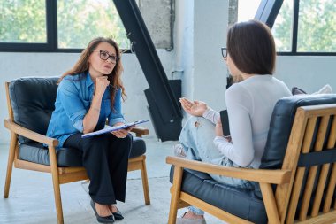 Orta yaşlı, kendine güvenen profesyonel kadın psikolog psikoterapist danışman ofiste birlikte oturan genç bir kadınla çalışıyor. Psikolojik hizmetler, bireysel terapi desteği