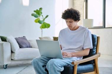 Evdeki sandalyede oturan yakışıklı ve ciddi bir erkeğin portresi. 20 yaşında bilgisayar başında yazı yazan kıvırcık bir öğrenci. Yaşam tarzı, eğitim, teknoloji, gençlik kavramı