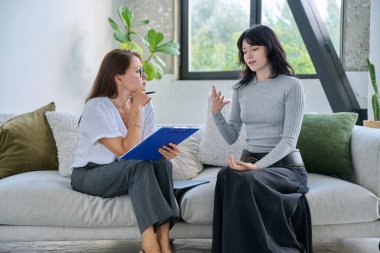 Terapi seansındaki genç bayan hasta kadın psikolog psikoterapist, akıl sağlığı danışmanı, birlikte kanepede oturan sosyal psikolog ile konuşuyor. Psikoloji Destek Servisi