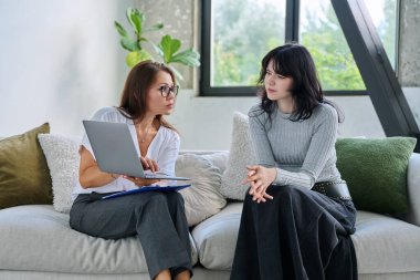 Terapi seansındaki genç kadın hasta kadın psikolog psikolog, ruh sağlığı danışmanı, sosyal psikolog dizüstü bilgisayarla birlikte kanepede oturuyor.