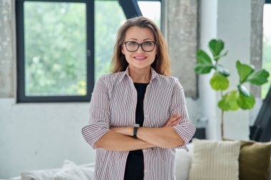 Kollarını kavuşturup poz veren kendinden emin orta yaşlı bir kadın portresi. Ofiste başarılı ve olgun bir bayan.