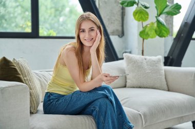 Kanepede oturan akıllı telefonlu genç bir kadının portresi. Evin içindeki kameraya bakıyor. Üniversite öğrencisi sınav için hazırlanıyor. Kadın dinleniyor. İnternet üzerinden alışveriş yapıyor.