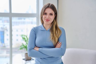 İç mekanda kollarını kavuşturarak poz veren kendinden emin genç bir kadının portresi. Gülümseyen mutlu 20 'li yaşlarda, sarışın, uzun saçlı, kameraya bakan bir kadın. Güzellik sağlık yaşam tarzı gençlik kavramı