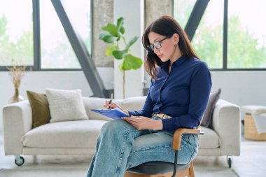 Ofisinde panosu olan kendine güvenen bir kadın sandalyede oturuyor. Ciddi kadın psikolog psikoterapist danışman sosyal hizmet uzmanı yönetici öğretmen eğitmen iş kadını