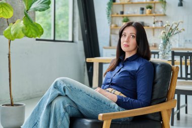 Evdeki sandalyede oturan üzgün, mutsuz genç bir kadın. Depresyon, stres, acı, sorunlar, akıl sağlığı insanları kavramı