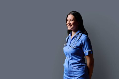 Gri stüdyo arka planında steteskop bulunan mavi üniformalı kadın doktor portresi, fotokopi odası. Tıp, insanlar, sağlık personeli, sağlık hizmetleri kavramı