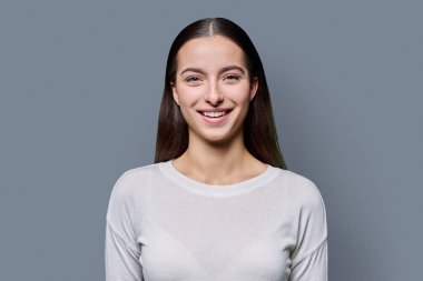 Gri stüdyo arka planında gülümseyen güzel bir genç kadının portresi. Kameraya bakan uzun siyah saçlı 18 yaşında başarılı bir kadın. Güzellik yaşam tarzı sağlık gençlik kavramı