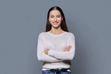 Kollarını kavuşturup gri stüdyonun arka planında kameraya bakan kendine güveni tam genç bir kız. Başarılı genç kız öğrenci üniversite yaşı gençlik için reklam ürünleri ve hizmetleri