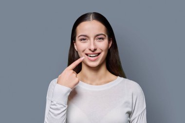 Gri arka planda, kamerada sağlıklı beyaz dişler gösteren güzel, mutlu, gülümseyen genç bir kadın. Diş sağlığı, tedavi, diş bakımı, oral sağlık kavramı
