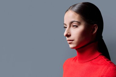 Gri arka planda genç ciddi bir kadının portresi. Kırmızılı güzel, düşünceli kadın ileriye bakıyor. Reklam metni için mekanı kopyalıyor. Gençlik servisi moda eğitimi kavramı