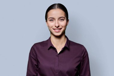 Gri stüdyo arka planında gülümseyen güzel bir genç kadının portresi. Kameraya bakan 18 yaşında başarılı bir kız. Güzellik yaşam tarzı sağlık gençlik kavramı
